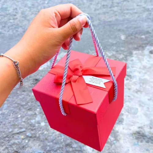 Hộp quà giấy vuông đỏ nắp rời, quai xách, có hoa kim tuyến, rơm và đèn đom đóm